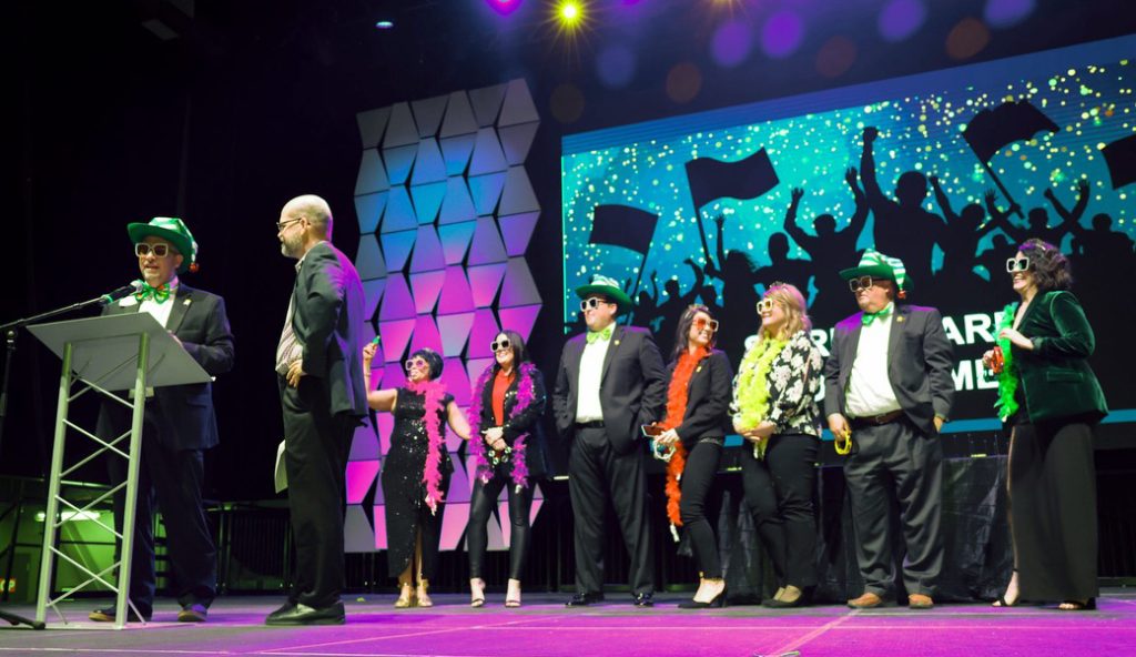 Bankers from FNBT stand in costume on stage while CEO John Gorton receives award.